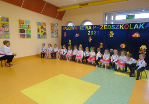 Grupa dzieci siedzi na krzesełkach, naprzeciwko dzieci siedzi Pani dyrektor Maria Królikowska, która rozmawia z dziecmi.